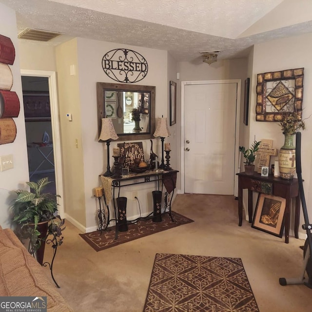 carpeted entrance foyer with baseboards, visible vents, and a textured ceiling