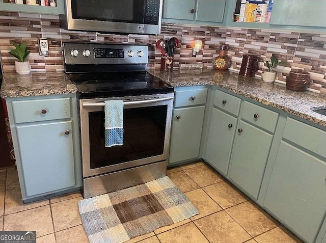 kitchen featuring light tile patterned floors, stainless steel appliances, green cabinetry, and decorative backsplash