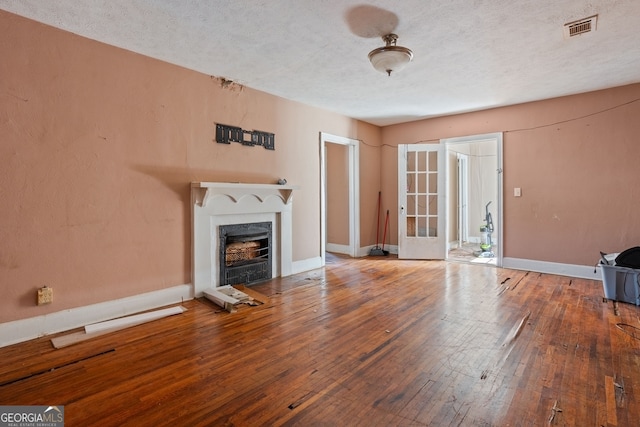 unfurnished living room with a textured ceiling, hardwood / wood-style flooring, a fireplace, visible vents, and baseboards