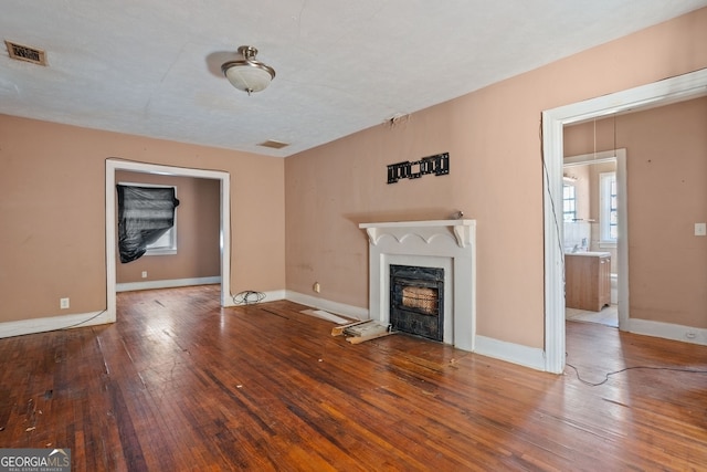 unfurnished living room featuring a fireplace with flush hearth, wood-type flooring, visible vents, and baseboards