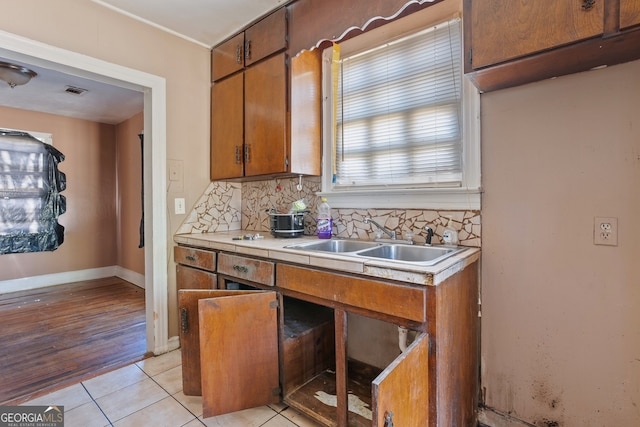 kitchen featuring brown cabinetry, light countertops, a sink, and tasteful backsplash