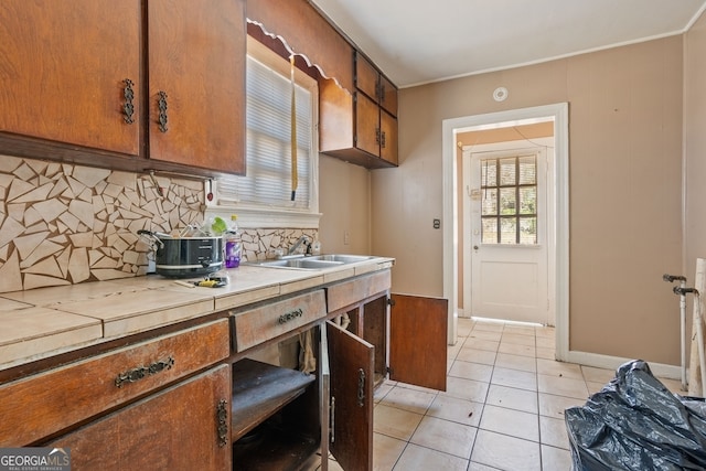 kitchen with tile countertops, light tile patterned flooring, a sink, decorative backsplash, and brown cabinets