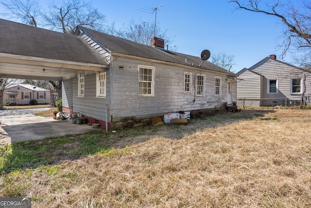 back of property with aphalt driveway, a chimney, an attached carport, and a lawn