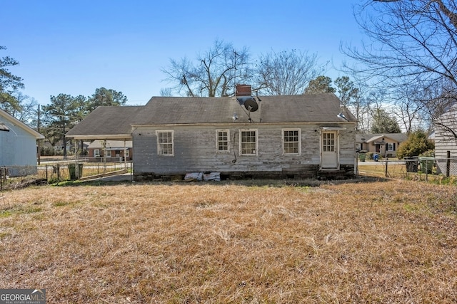 rear view of house featuring entry steps, a chimney, fence, and a yard