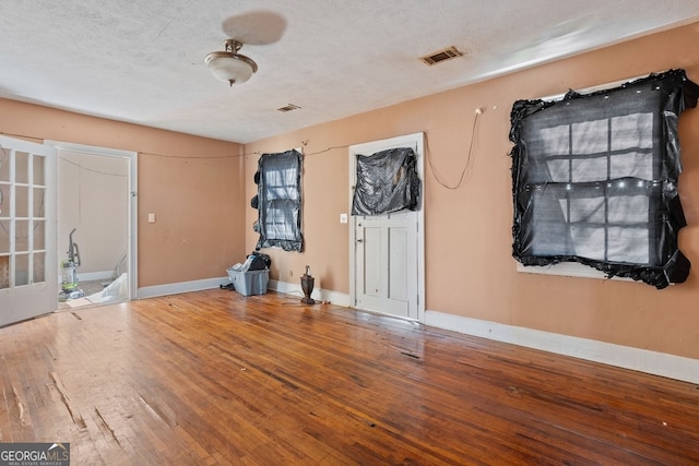 empty room with a textured ceiling, hardwood / wood-style floors, visible vents, and baseboards