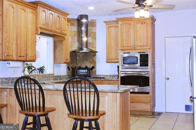 kitchen with crown molding, a breakfast bar area, light tile patterned floors, stainless steel appliances, and wall chimney range hood