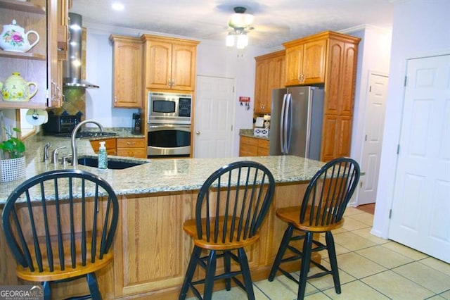 kitchen with stainless steel appliances, a peninsula, a sink, wall chimney range hood, and light stone countertops