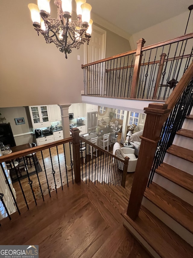 stairs with a high ceiling, wood finished floors, and ornate columns