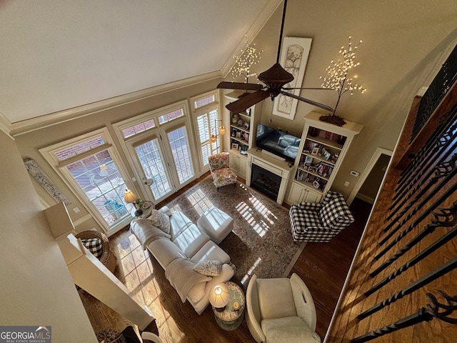 living area featuring a high ceiling, a fireplace, wood finished floors, baseboards, and crown molding