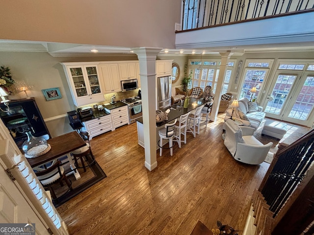 living room with crown molding, decorative columns, a towering ceiling, and wood finished floors