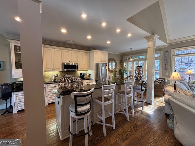 kitchen with dark countertops, dark wood-style floors, ornamental molding, stainless steel appliances, and ornate columns