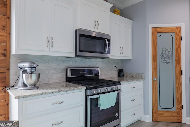 kitchen with light stone countertops, stainless steel appliances, crown molding, white cabinetry, and backsplash