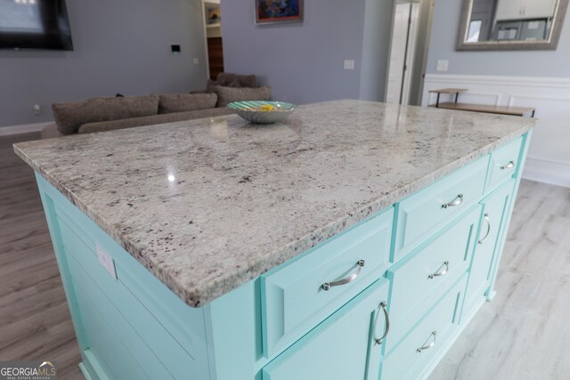 kitchen with light stone countertops, light wood-style flooring, a kitchen island, and wainscoting