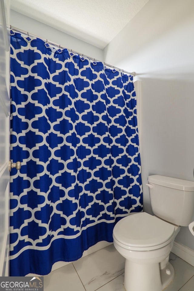 bathroom featuring toilet, marble finish floor, curtained shower, and a textured ceiling