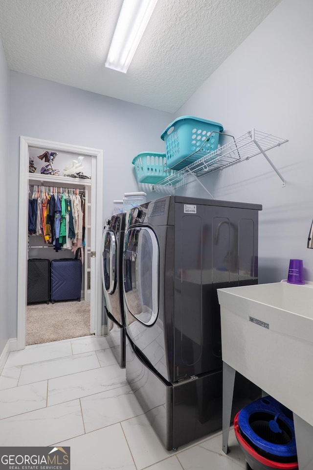 clothes washing area featuring marble finish floor, washing machine and clothes dryer, a sink, a textured ceiling, and laundry area