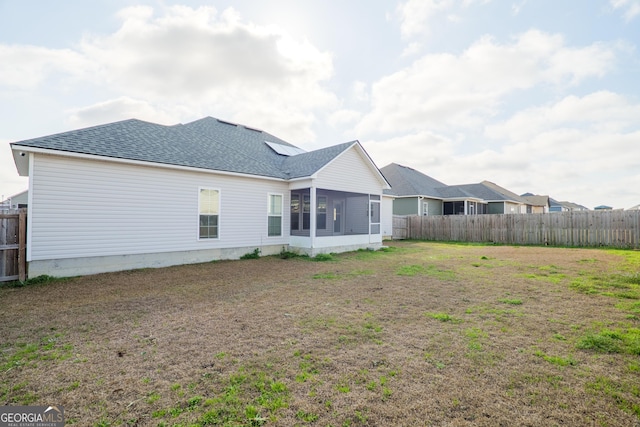 back of property with a sunroom, a fenced backyard, a shingled roof, and a yard