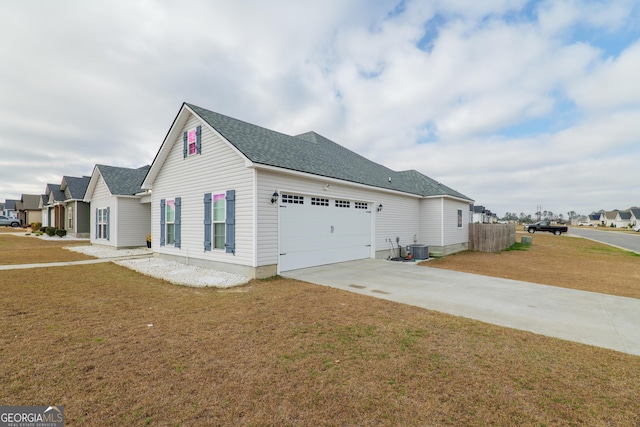 view of side of property with driveway, roof with shingles, an attached garage, cooling unit, and a yard