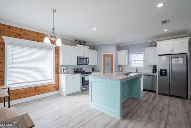 kitchen with a center island, stainless steel appliances, visible vents, ornamental molding, and white cabinetry