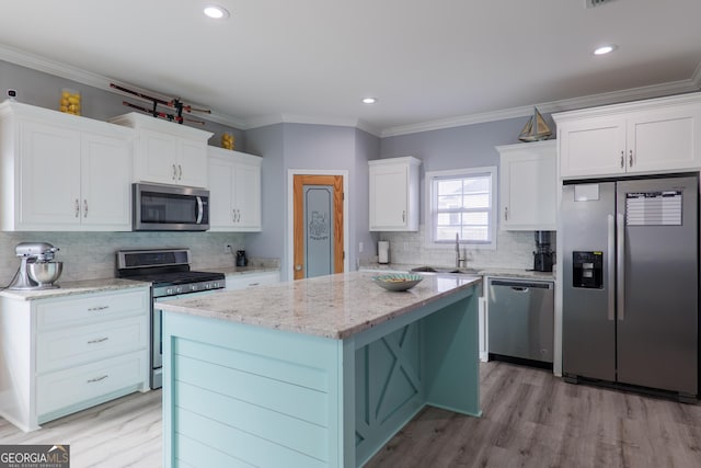 kitchen with white cabinets, ornamental molding, appliances with stainless steel finishes, a center island, and light wood finished floors