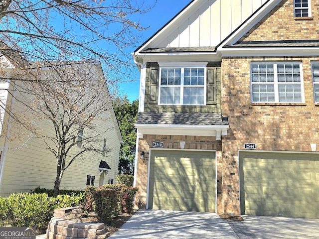 view of front of home featuring driveway, roof with shingles, an attached garage, board and batten siding, and brick siding