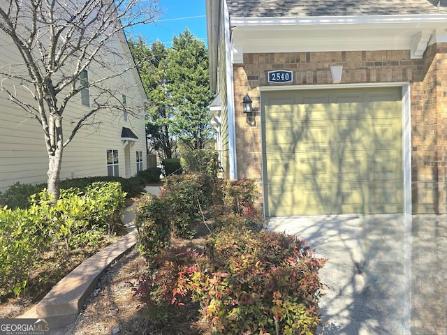 exterior space with a garage, brick siding, and roof with shingles