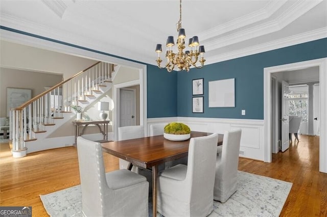 dining area featuring wood finished floors, stairs, wainscoting, a tray ceiling, and an inviting chandelier