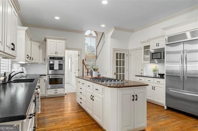 kitchen featuring dark countertops, white cabinets, a sink, and built in appliances