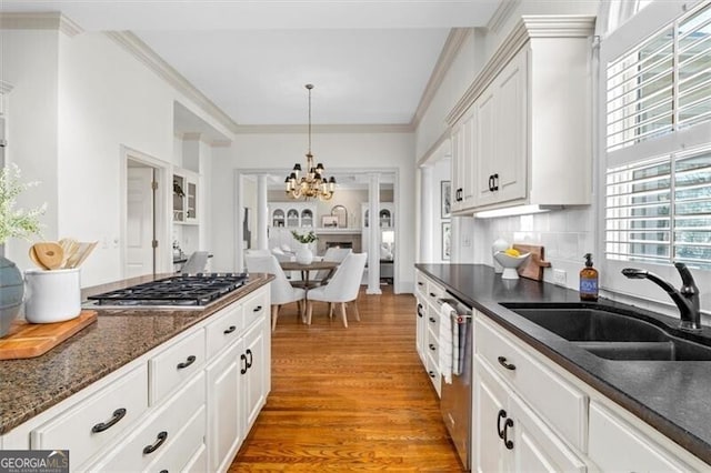 kitchen with appliances with stainless steel finishes, ornamental molding, light wood-type flooring, white cabinetry, and a sink