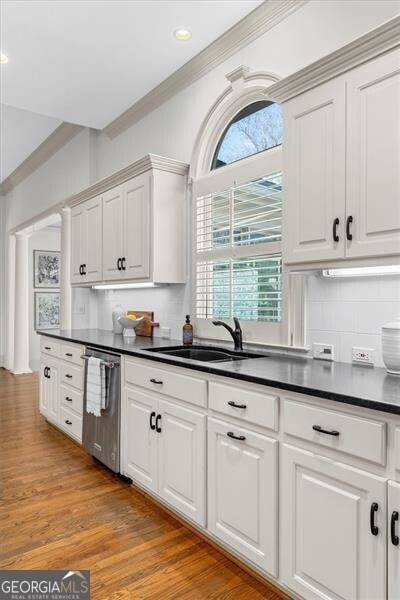 kitchen featuring a sink, white cabinets, light wood-style floors, dishwasher, and dark countertops