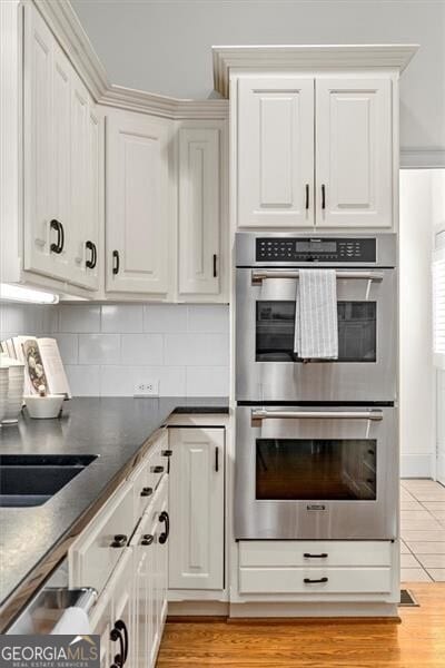 kitchen featuring stainless steel double oven, white cabinetry, and backsplash