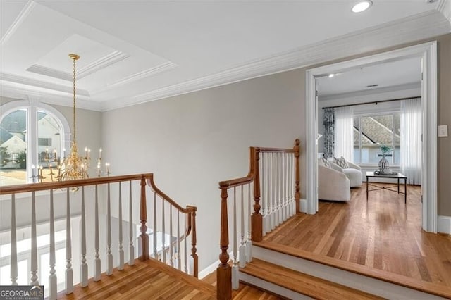 corridor with a chandelier, ornamental molding, wood finished floors, and an upstairs landing