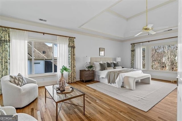 bedroom with ceiling fan, a tray ceiling, wood finished floors, and visible vents