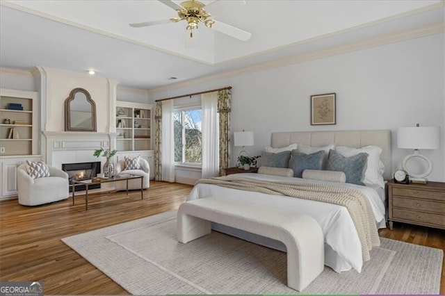 bedroom featuring crown molding, a ceiling fan, wood finished floors, and a glass covered fireplace