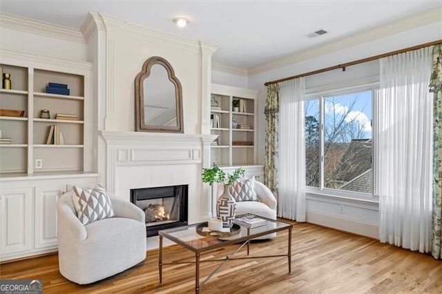 living area with baseboards, visible vents, ornamental molding, light wood-style floors, and a fireplace