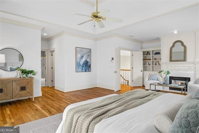 bedroom with a glass covered fireplace, crown molding, baseboards, and wood finished floors