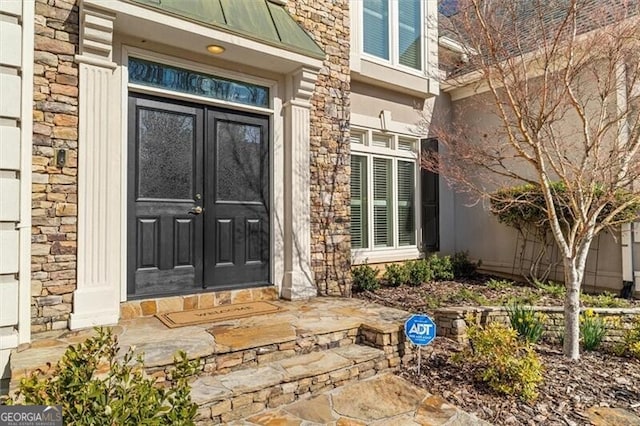 doorway to property with stone siding, metal roof, a standing seam roof, french doors, and stucco siding