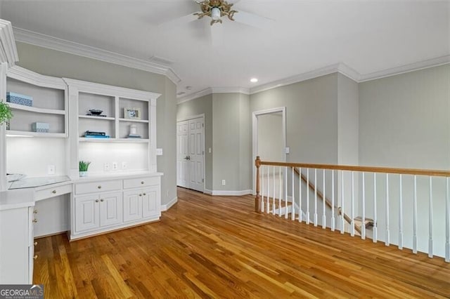 interior space with built in study area, crown molding, open shelves, and wood finished floors