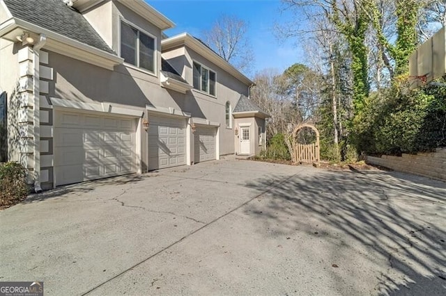 view of side of property featuring a garage, concrete driveway, a shingled roof, and stucco siding