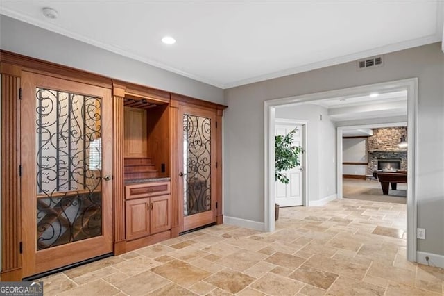 foyer entrance with ornamental molding, stone tile flooring, visible vents, and baseboards