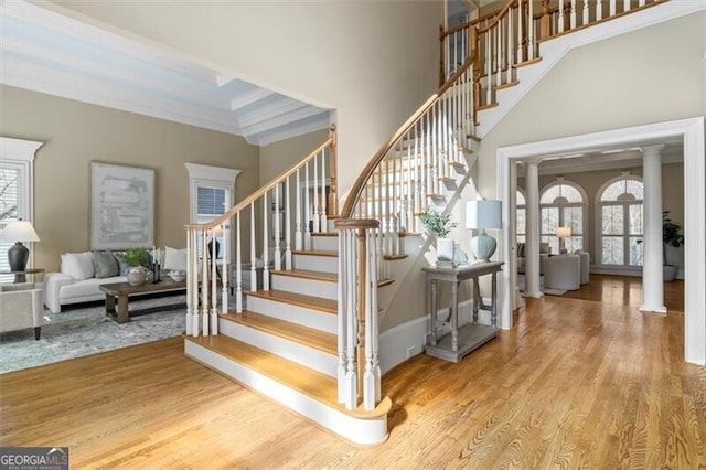 stairway featuring a towering ceiling, decorative columns, crown molding, and wood finished floors