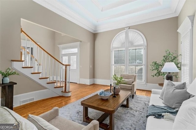 living room featuring visible vents, ornamental molding, wood finished floors, stairs, and a tray ceiling