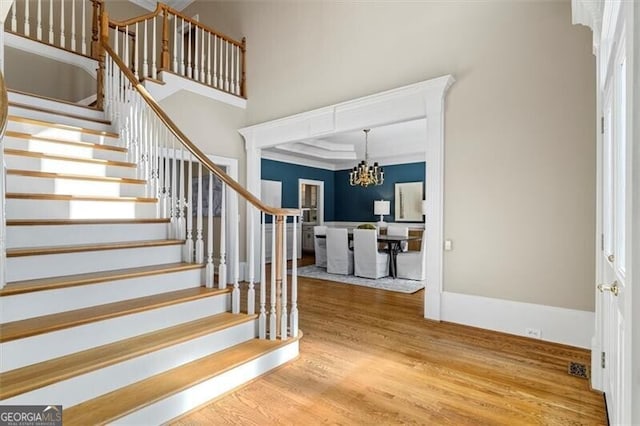 foyer entrance with wood finished floors, a towering ceiling, baseboards, stairway, and an inviting chandelier