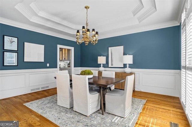 dining space with wood finished floors, a raised ceiling, visible vents, and a notable chandelier