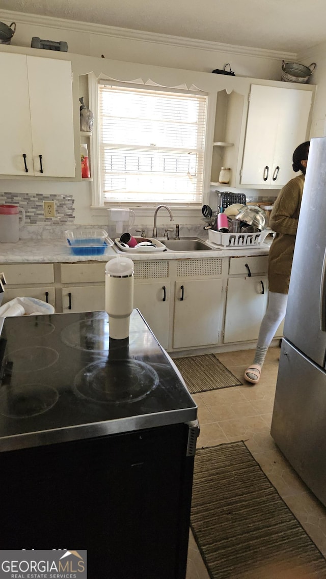 kitchen with a sink, white cabinetry, light countertops, freestanding refrigerator, and open shelves