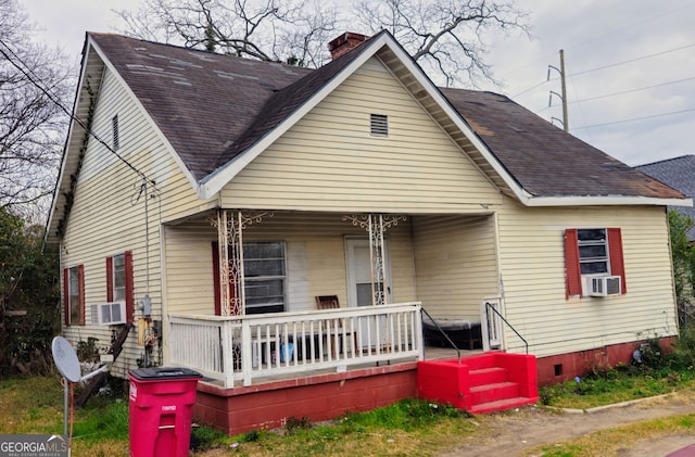 view of front of home featuring a porch, cooling unit, a shingled roof, and a chimney