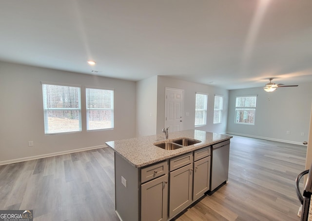 kitchen with gray cabinets, stainless steel dishwasher, open floor plan, a kitchen island with sink, and a sink