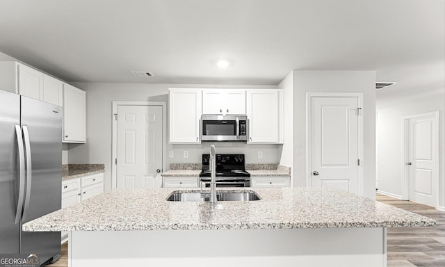 kitchen with stainless steel appliances, white cabinets, visible vents, and a center island with sink