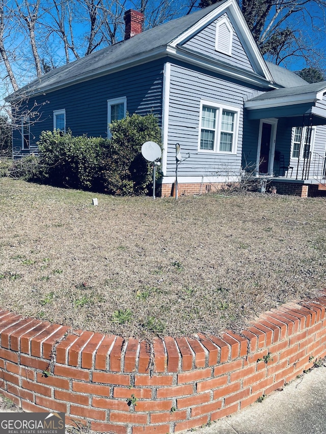 view of side of home featuring covered porch, a yard, and a chimney