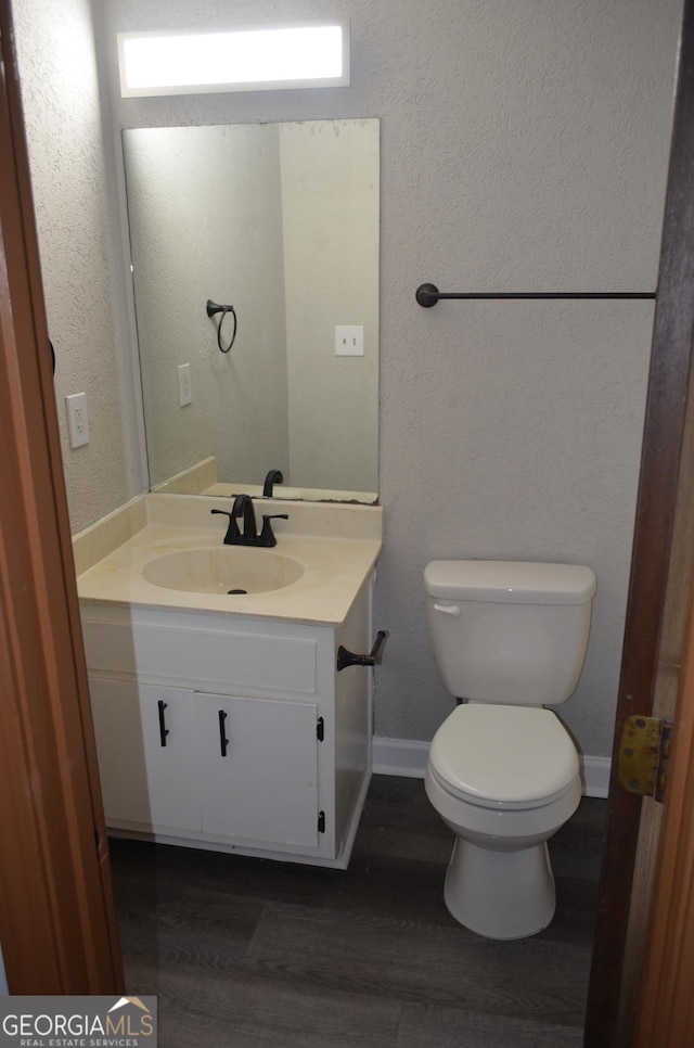 bathroom with a textured wall, toilet, vanity, wood finished floors, and baseboards