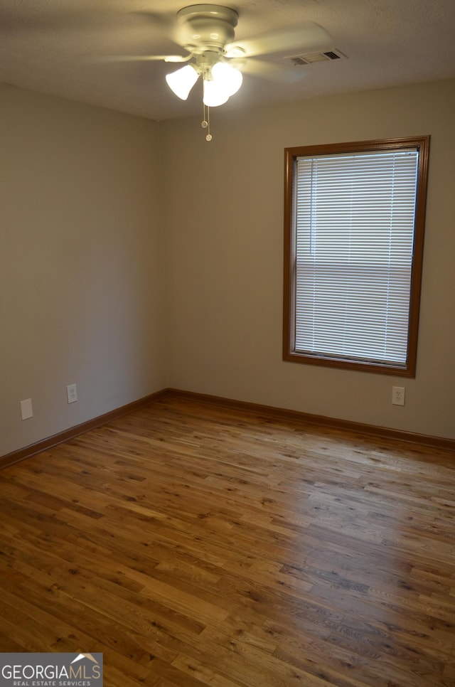 unfurnished room featuring a ceiling fan, visible vents, baseboards, and wood finished floors